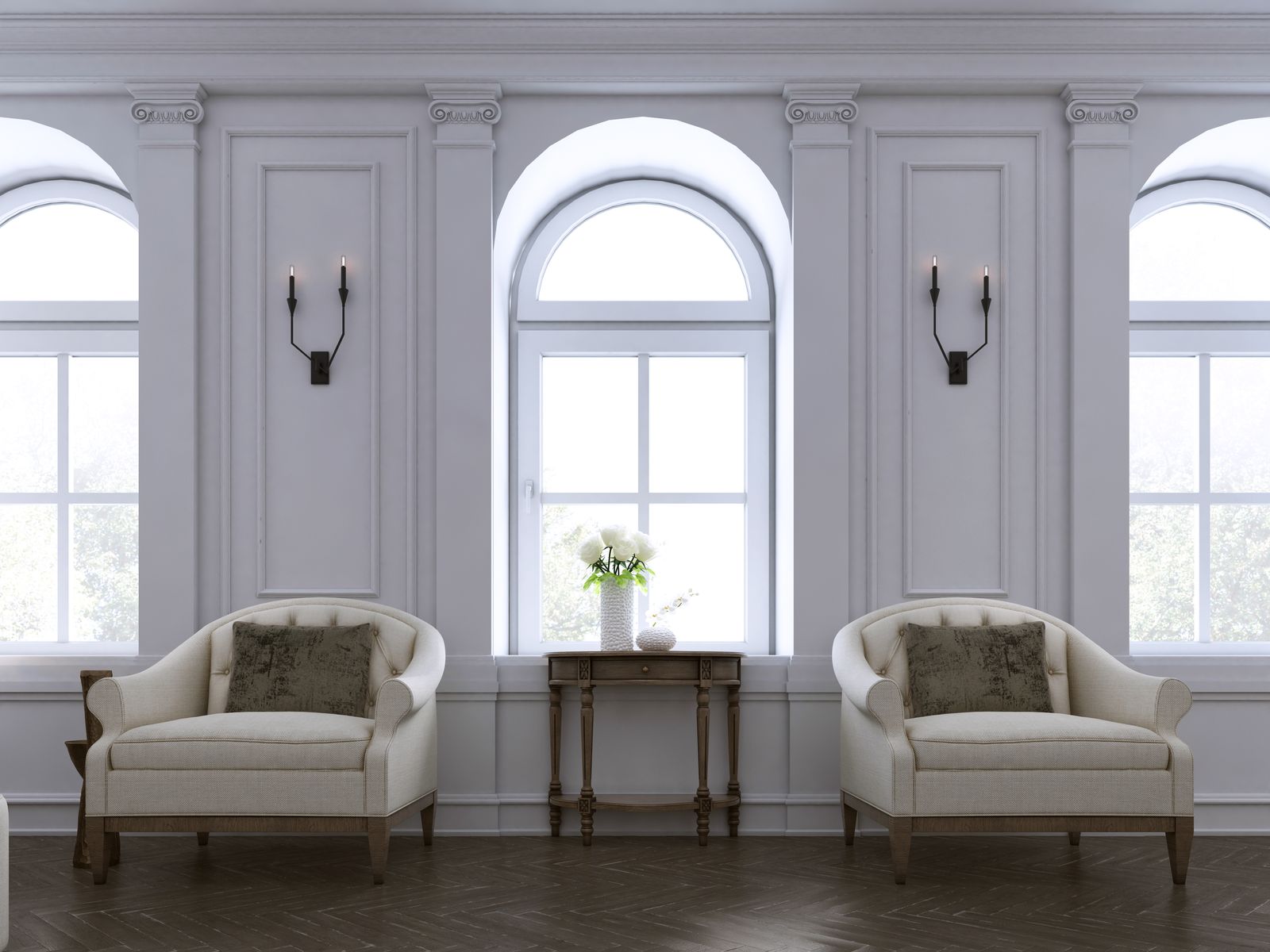 A modern traditional room with paneled walls, pilasters and arched windows, a pair of cream tub chairs with olive pillows, a carved wood console and iron candle sconces